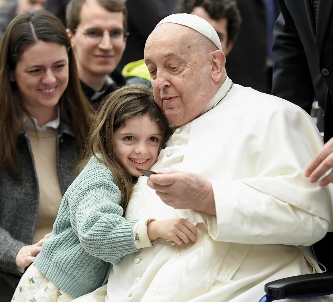A young girl and Pope Francis share smiles and hugs.